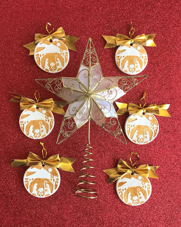 six gold-stamped nativity ornaments surrounding a Christmas tree star