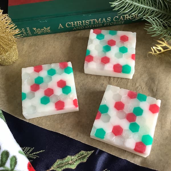 three square bars of soap covered in white, green, red and glitter hexagonal mosaic tiles