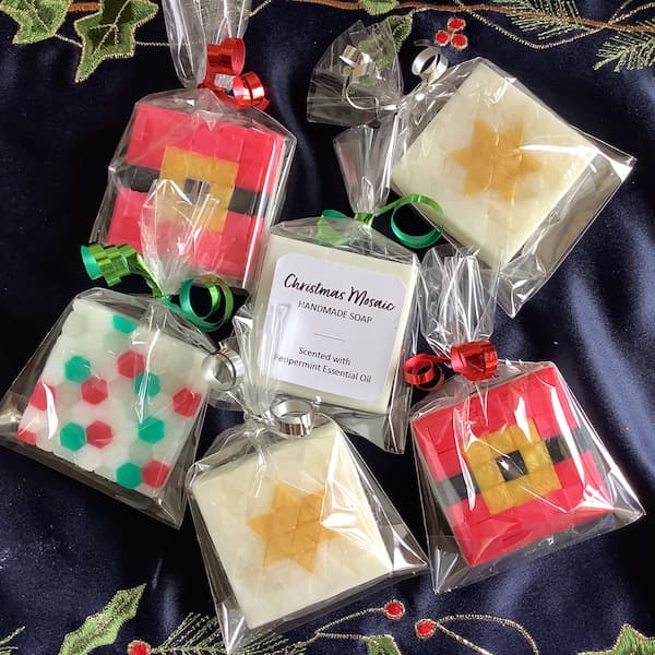 six square mosaic Christmas soap bars wrapped in cellophane bags with Christmas coloured ribbon. one of them has a plain white label on the back.