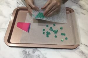 two hands removing green hexagonal mosaic tiles from a silicone mould