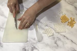 a pair of hands using a sharp knife to cut up soap mosaic tiles
