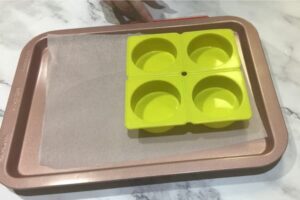 a four cavity round soap mould sitting on a paper-lined tray on top of a set of kitchen scales