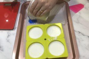 pouring royal blue soap base from a paper cup into a hexagon-shaped mosaic tile mould