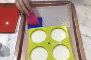 using a rubber scraper to push blue soap base into small mosaic tile mould cavities