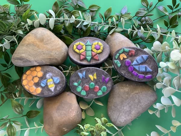 four oval shaped, black bars of soap with bright and colourful garden insect mosaics on them