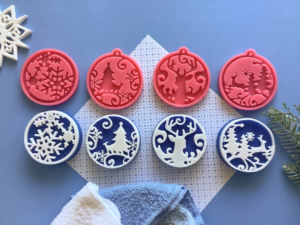 four Christmas ornaments silicone moulds in a row with a row of soap bars with identical patterns underneath