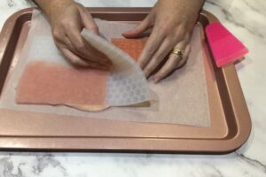 two hands peeling back a soap mould from a slab of mosaic soap tiles