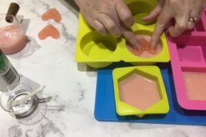 a pair of hand pressing a heart shaped soap embed into a bar of soap