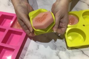two hands pushing a soap bar out of a soap mould