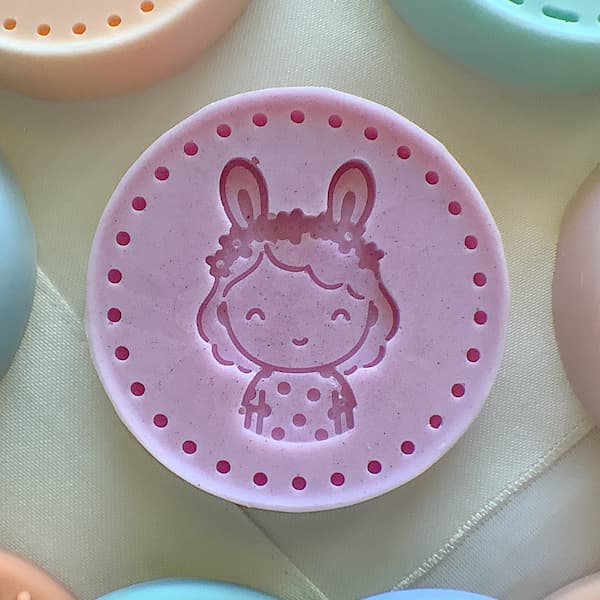 a mauve round soap bar with an imprint of a girl wearing bunny ears
