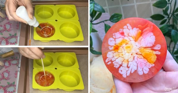 A three‑panel collage demonstrating a bloom technique in melt and pour soap making. The two panels on the left show a hand adding and swirling white colour into orange soap inside a round cavity of a bright green silicone mould. The panel on the right shows the finished round soap held in a hand, featuring a dramatic carnation flower‑like bloom pattern with white, yellow, and orange petals radiating from the centre against a translucent coral‑pink background. Soft towels, a bath sponge, green leaves, and a neutral textured surface create a spa‑inspired presentation.
