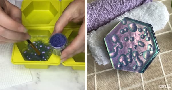 A side‑by‑side collage demonstrating a raindrop resin‑inspired soap technique. On the left, a hand brushes purple pigment onto clear soap inside a bright green hexagonal silicone mould, with small round droplets scattered on the surface. On the right, a finished hexagonal soap in shimmering blue‑green and purple tones features raised bubble‑like droplets, creating the appearance of water droplets on glass. Folded white and lavender towels surround the soap, adding a soft spa‑style touch.