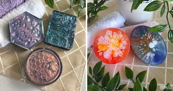 A collage showcases five completed melt and pour soaps inspired by popular resin art techniques. On the left are three soaps: a hexagonal soap with a rain drop effect in shimmering purple and blue tones, a rectangular soap with a crumpled metallic texture resembling crushed velvet, and a round honeycomb soap featuring a detailed bee design. On the right are two round soaps: one with a dramatic white‑and‑orange floral bloom pattern radiating from the centre, and another with an organic petri‑dish effect created by streaks of blue, white, copper, and brown. The soaps are displayed on a neutral textured surface with soft towels and green leafy stems, creating an elegant spa‑style presentation.